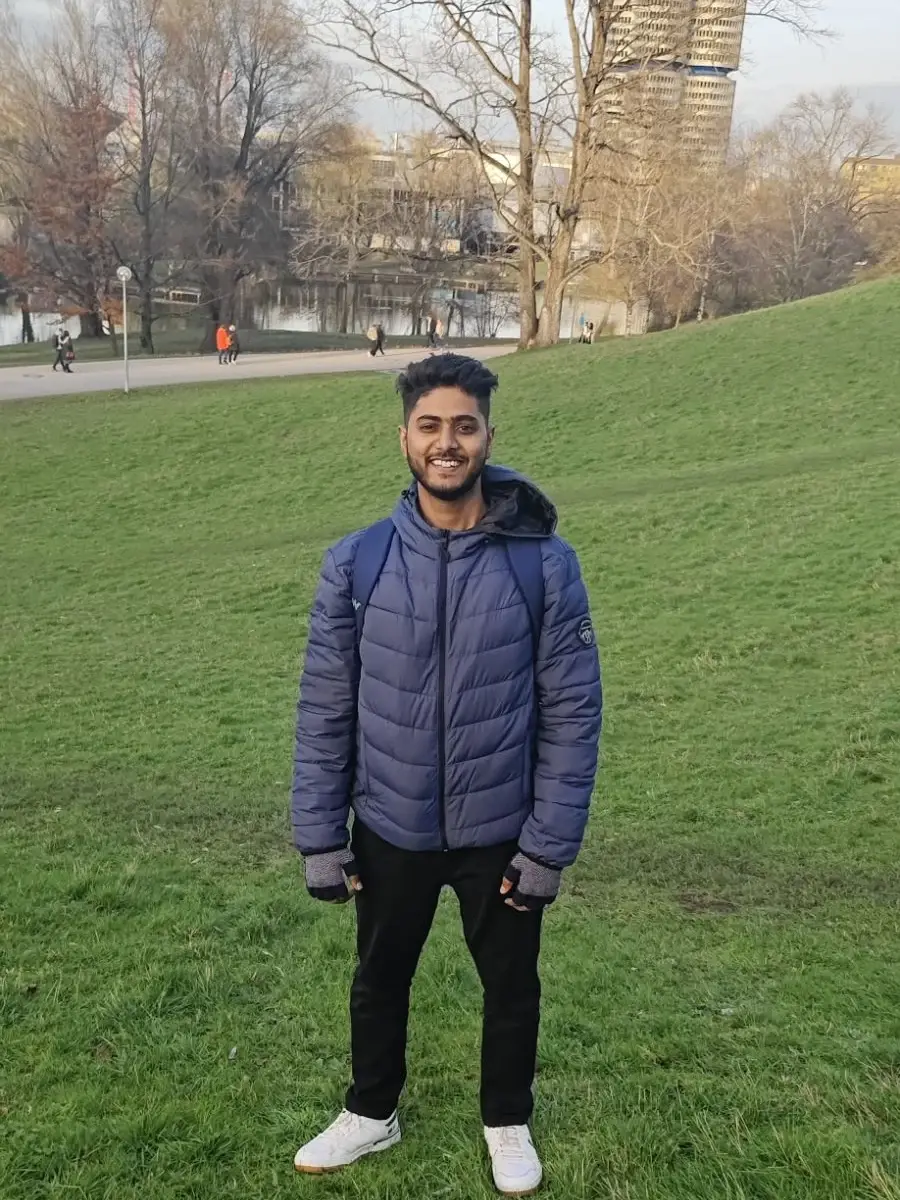 Suprabhat Kumar smiling in a navy puffer jacket on a grassy park hill, with bare winter trees and a city skyline behind him.